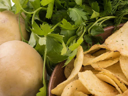 Closeup of crispy potato chips with fresh greens as a background. Junk food concept. Top view of a fast snack.の写真素材