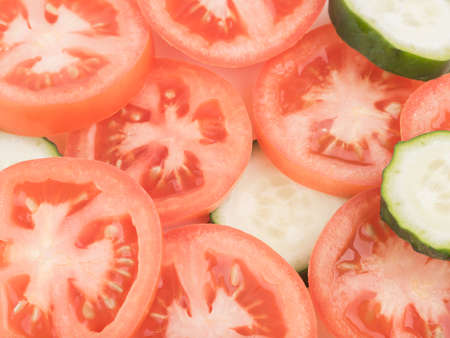 A top view of sliced green cucumbers and red tomatoes as a background, closeup. A concept of fresh vegetables for saladsの写真素材