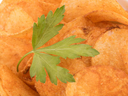 Closeup of crispy potato chips with fresh parsley as a background. Junk food concept. Top view of a fast snack.の写真素材
