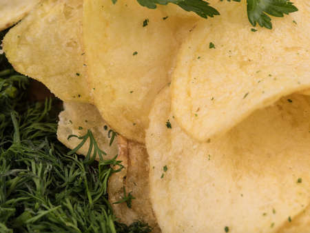 Closeup of crispy potato chips with fresh greens as a background. Junk food concept. Top view of a fast snack.の写真素材