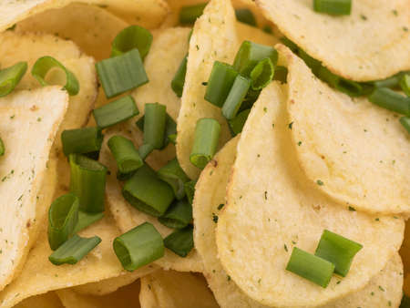 Closeup of crispy potato chips with fresh greens as a background. Junk food concept. Top view of a fast snack.の写真素材