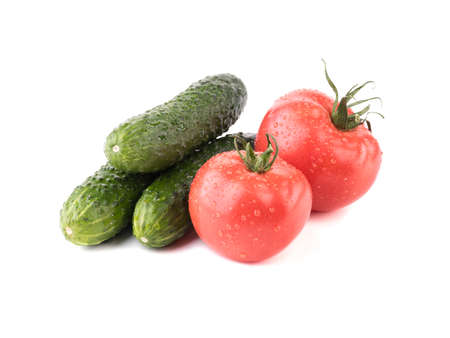 A closeup of fresh autumn vegetables isolated on a white background. A group of green cucumbers, juicy and red tomatoes. Ingredients for saladの写真素材
