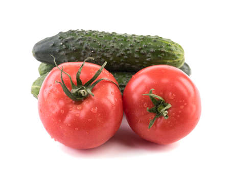 A closeup of fresh autumn vegetables isolated on a white background. A group of green cucumbers, juicy and red tomatoes. Ingredients for saladの写真素材