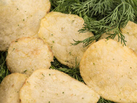 Closeup of crispy potato chips with fresh greens as a background. Junk food concept. Top view of a fast snack.の写真素材