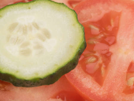 A top view of sliced green cucumbers and red tomatoes as a background, closeup. A concept of fresh vegetables for saladsの写真素材