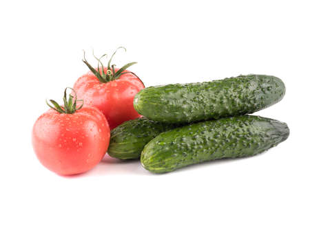A closeup of fresh autumn vegetables isolated on a white background. A group of green cucumbers, juicy and red tomatoes. Ingredients for saladの写真素材