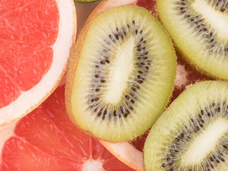 A red sliced grapefruit and fresh kiwi with seeds as background. A concept of citrus fruits full of vitaminsの写真素材