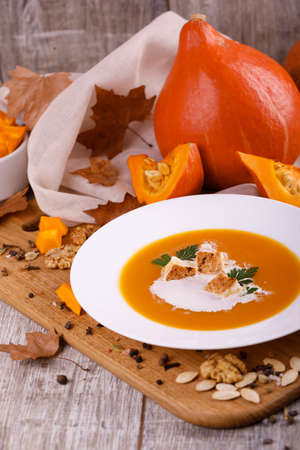 A composition of a plate of pumpkin cream-soup, pumpkins with seeds on a wooden background. Autumn harvest and Halloween concept.の写真素材