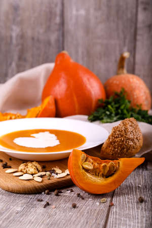 A composition of a plate of pumpkin cream-soup, pumpkins with seeds on a wooden background. Autumn harvest and Halloween concept.の写真素材
