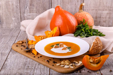A composition of a plate of pumpkin cream-soup, pumpkins with seeds on a wooden background. Autumn harvest and Halloween concept.の写真素材