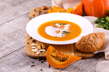 A composition of a plate of pumpkin cream-soup, pumpkins with seeds on a wooden background. Autumn harvest and Halloween concept.の写真素材