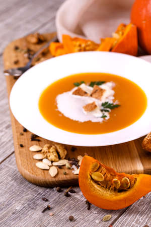 A composition of a plate of pumpkin cream-soup, pumpkins with seeds on a wooden background. Autumn harvest and Halloween concept.の写真素材