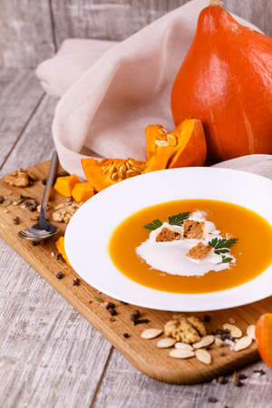 A composition of a plate of pumpkin cream-soup, pumpkins with seeds on a wooden background. Autumn harvest and Halloween concept.の写真素材