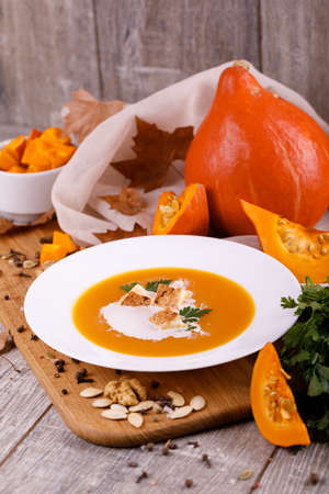A composition of a plate of pumpkin cream-soup, pumpkins with seeds on a wooden background. Autumn harvest and Halloween concept.の写真素材