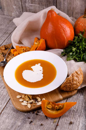 A composition of a plate of pumpkin cream-soup, pumpkins with seeds on a wooden background. Autumn harvest and Halloween concept.の写真素材