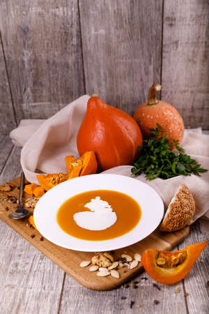 A composition of a plate of pumpkin cream-soup, pumpkins with seeds on a wooden background. Autumn harvest and Halloween concept.の写真素材