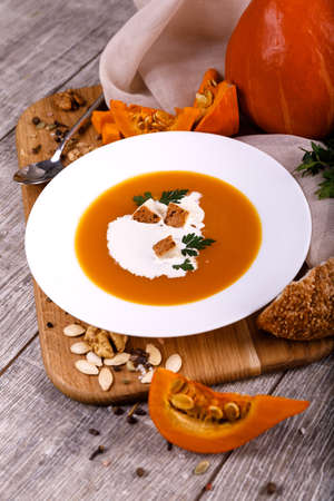 A composition of a plate of pumpkin cream-soup, pumpkins with seeds on a wooden background. Autumn harvest and Halloween concept.の写真素材