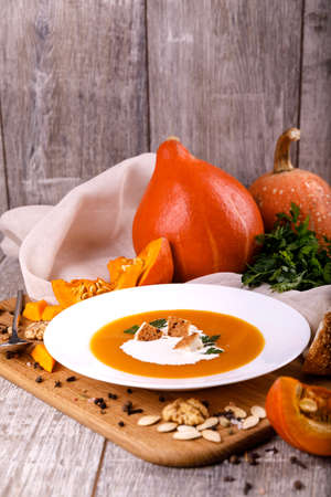 A composition of a plate of pumpkin cream-soup, pumpkins with seeds on a wooden background. Autumn harvest and Halloween concept.の写真素材