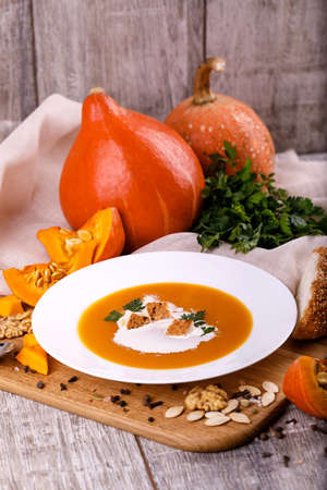 A composition of a plate of pumpkin cream-soup, pumpkins with seeds on a wooden background. Autumn harvest and Halloween concept.の写真素材