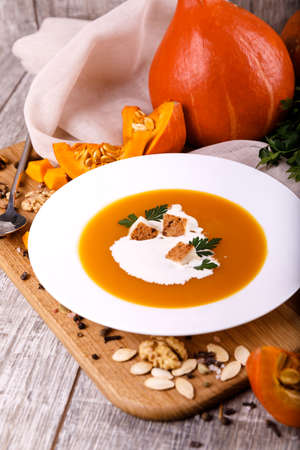 A composition of a plate of pumpkin cream-soup, pumpkins with seeds on a wooden background. Autumn harvest and Halloween concept.の写真素材