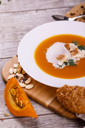 A composition of a plate of pumpkin cream-soup, pumpkins with seeds on a wooden background. Autumn harvest and Halloween concept.の写真素材