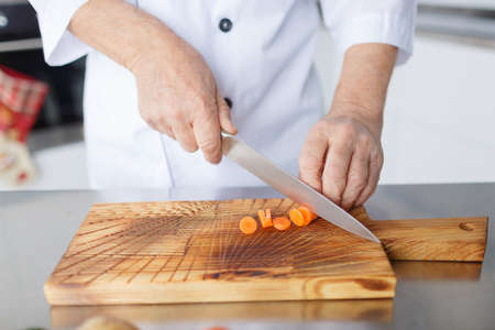 Man's hands with a knife slicing carrots for a dinner on a wooden board. Vegetables full of vitaminsの写真素材