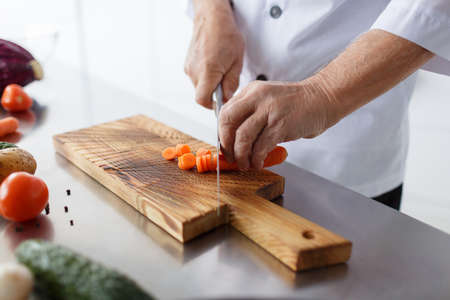 Man's hands with a knife slicing carrots for a dinner on a wooden board. Vegetables full of vitaminsの写真素材