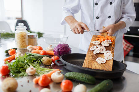 Man's hands with a knife slicing carrots and mushrooms for a dinner on a wooden board. Vegetables full of vitaminsの写真素材