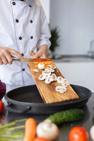 Man's hands with a knife slicing carrots and mushrooms for a dinner on a wooden board. Vegetables full of vitaminsの写真素材