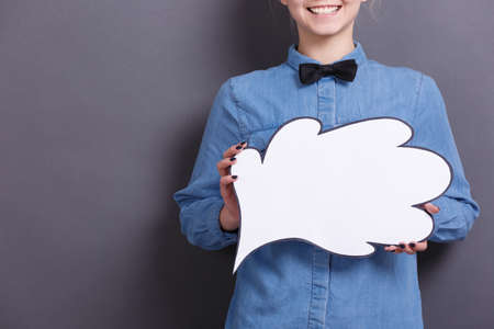The young businesswoman with smile holds white paper cloud on a gray background. A woman with business ideas and thoughts concept.の写真素材