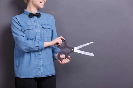 A young woman with big paper scissors on a gray background. A concept of objects for work with documents.の写真素材