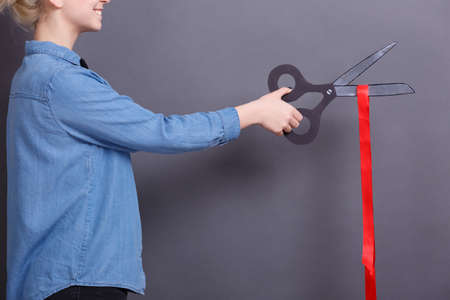 A young woman with big paper scissors and red ribbon on a gray background. A concept of objects for work with documents.の写真素材