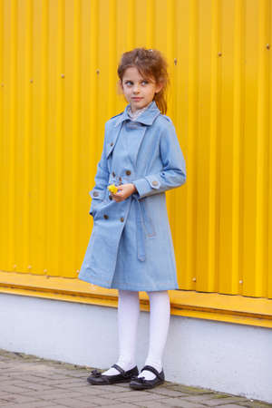 A pretty little girl in a blue denim coat on a bright yellow background. Fall fashion clothes for kids concept.の写真素材