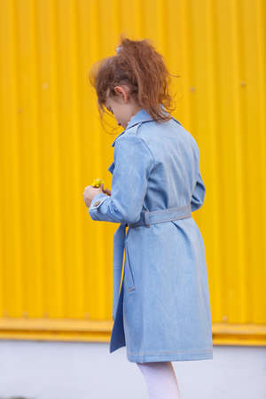 A cute little girl in a blue denim coat on a bright yellow background. Fall fashion clothes for kids concept.の写真素材