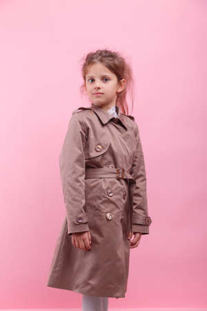Portrait of a smiling little girl in an autumn coat on a pink background. Childrens autumn clothes concept.の写真素材