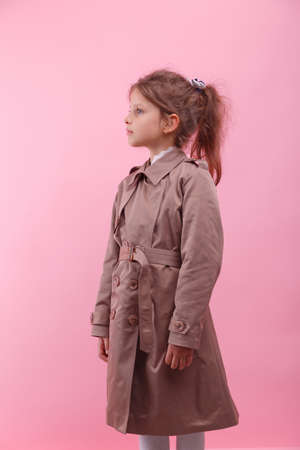 Portrait of a smiling little girl in an autumn coat on a pink background. Childrens autumn clothes concept.の写真素材