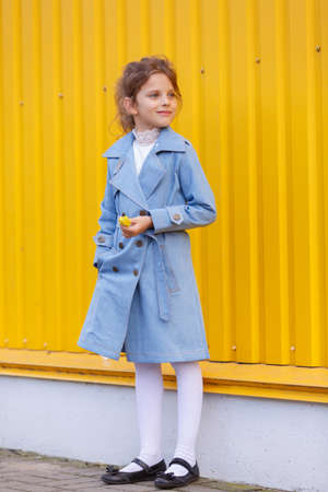 A cute little girl in a blue denim coat on a bright yellow background. Fall fashion clothes for kids concept.の写真素材