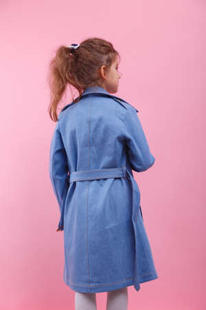 A back of a little girl in a blue denim coat on a pink background. Fall and spring fashion concept.の写真素材
