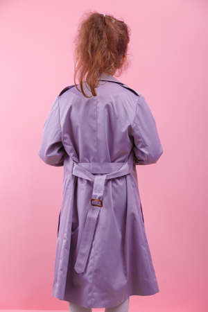 A back of a little girl in a purple coat on a pink background. Fall and spring fashion concept.の写真素材