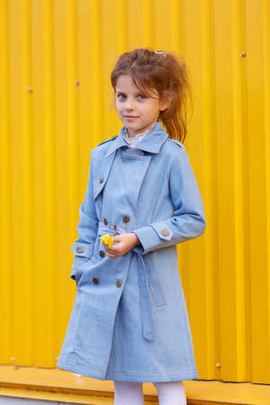 A beautiful little girl in a blue denim coat on a bright yellow background. Fall fashion clothes for kids concept.の写真素材