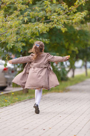 A happy little girl in an autumn coat running and having fun in the park. Autumn concept.の写真素材