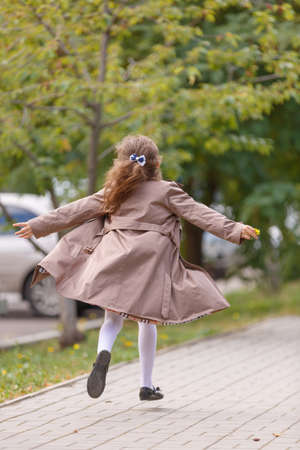 A happy little girl in an autumn coat running and having fun in the park. Autumn concept.の写真素材