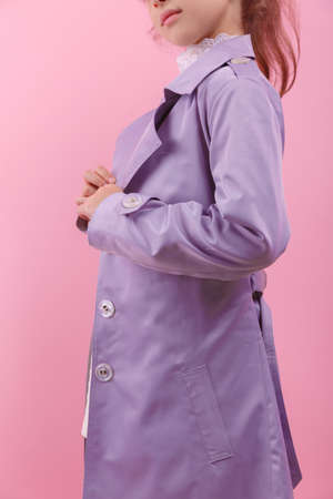 Close-up portrait of a cute little girl in a violet coat on a pink background. Childrens autumn clothes concept.の写真素材