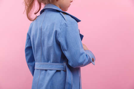 A back of a schooler girl in a blue denim coat on a bright pink background, close-up. Fall and spring children's fashion concept.の写真素材