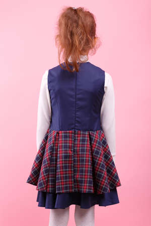 A back of girl in a school uniform on a bright pink background, close-up. Education, school concept.の写真素材