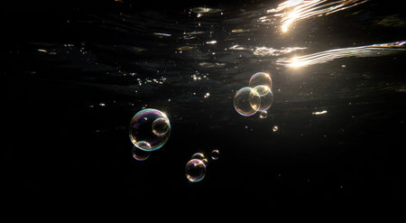 Underwater view, several iridescent bubbles ascend against a dark, sunlit backgroundの素材