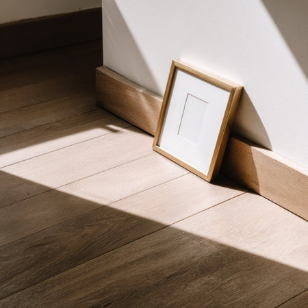 A picture frame rests against a wall, casting a long shadow on wooden flooringの素材