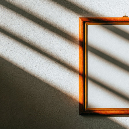 A framed blank picture on a white wall with harsh shadows from blindsの素材