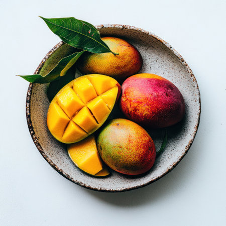 A plate of fresh mangoes, with one sliced and cut into small pieces on the left side of the bowl. The background is white, with high-definition photography details. This photo was taken using a Canon camera, with clear focus and bright colors. It has a strong contrast between light and dark. There are no other fruits in front of it. In the style of Japanese art, there are green leaves hanging from the mango. --v 6.1 Job ID: 85b11e6d-908f-4f6d-9a93-4b6e0c28e1bcの素材