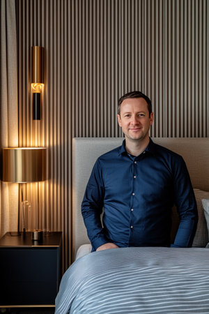 A modern bedroom with an elegant bed, featuring navy blue and grey stripes on the fabric cover. The wall behind is adorned with vertical wood strips in shades of gold and brown, creating a luxurious atmosphere. A sleek bedside table stands beside it, illuminated by soft lighting from lamps that add warmth to the space. This setting captures a sophisticated ambiance perfect for sleeping at night. --ar 2:3 --v 6.1 Job ID: b8866982-1f1f-41f1-9b9c-db33119e2ca3の素材